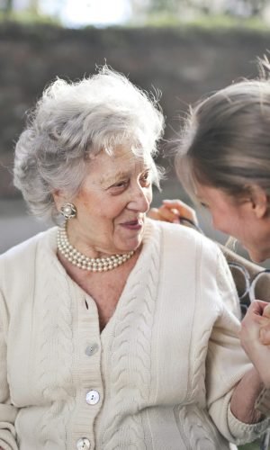 Joyful interaction between an elderly woman and her granddaughter in a sunny outdoor setting.